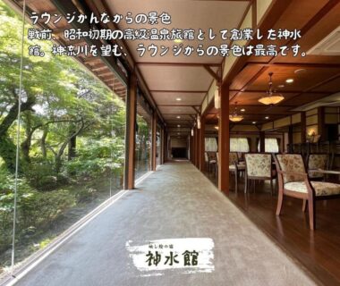 Long wooden corridor with glass wall overlooking lush garden and seating area at Shinsuikan in Gunma