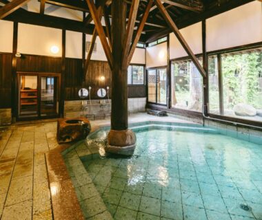 Indoor onsen bath with wooden beams, tiled pool and large windows at Kamikura Matsurube Onsen in Iwate