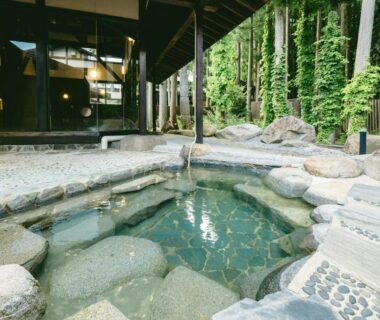Stone onsen bath with clear water under timber eaves and forest backdrop at Kamikura, Matsurube Onsen, Iwate