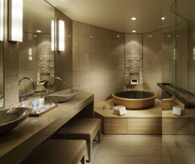 Indoor bathroom with round wooden soaking tub, stone tile walls and dual sinks at Chikusenso Onsen, Miyagi