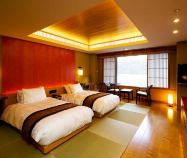 Tatami room with low twin beds, shoji screens, seating area and warm wooden accents at Chikusenso Onsen, Miyagi