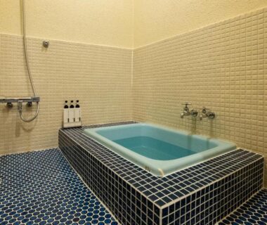 Indoor tiled bathing room with raised soaking tub, wall-mounted shower and toiletry bottles on ledge