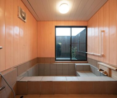 Interior bathing room with tiled soaking tub and wooden paneling at 素泊り旅館 Yururi in Ōita, Kyūshū