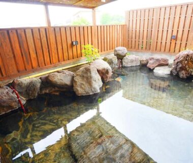 Rock-lined onsen bath with wooden fence at 素泊り旅館 Yururi in Ōita, Kyūshū