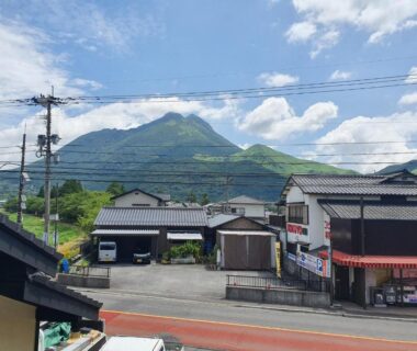 Street with tiled roofs and a green mountain backdrop near 素泊り旅館 Yururi in Ōita