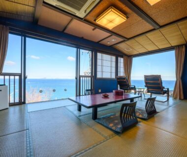 Tatami room at Shinpachiya with low table, floor chairs and large windows framing coastal view in Mie