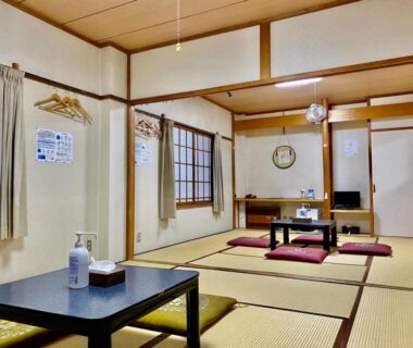 Spacious tatami room with low tables, zabuton cushions, shoji screens and hand sanitizer at Naeba Lodge Oka