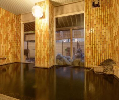 Tiled indoor onsen bath with spout and windows at Fukubikiya Hōraikan in Niigata's Yomogihira Onsen