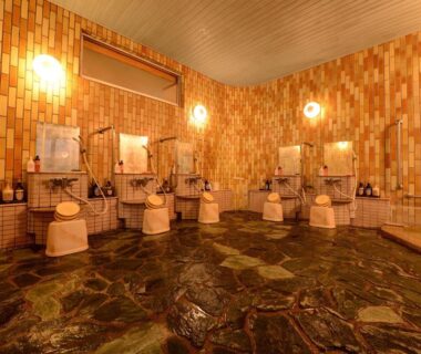 Tiled indoor onsen wash area with multiple shower stations at Hōraikan Yomogihira Onsen, Niigata