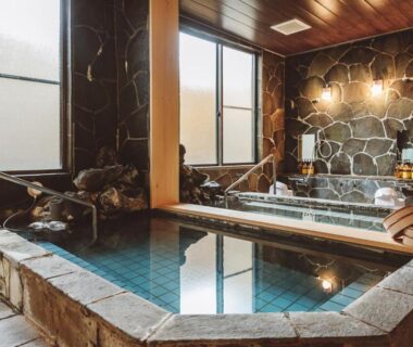 Indoor stone onsen bath with wooden accents at 蓼科BASE kitchen,spa&hotel in Nagano, Chūbu