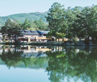 Lake reflection of ryokan building framed by pine trees and mountains at 蓼科BASE kitchen,spa&hotel in Nagano