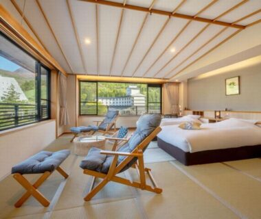 Tatami room with platform beds, wooden lounge chairs and large window overlooking greenery at Kinosato Zaō Onsen, Yamagata