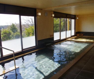 Indoor bath with large windows overlooking nearby water and shoreline at Kashikojima Park Hotel Michishio