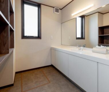 Bright communal wash area with long vanity, dual sinks, large mirror and wooden shelving at Isamiya ryokan in Fukushima