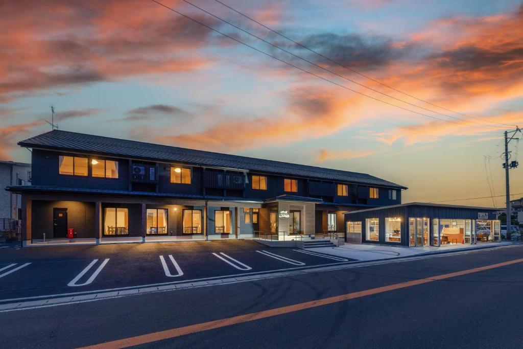 Sunset exterior of Isamiya auberge Fukushima Two-story Isamiya auberge building at dusk with lit windows and empty parking area along the road in Fukushima