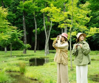 Two guests in hats walking by a pond amid lush trees at Nasu Muku no Ne Tochigi