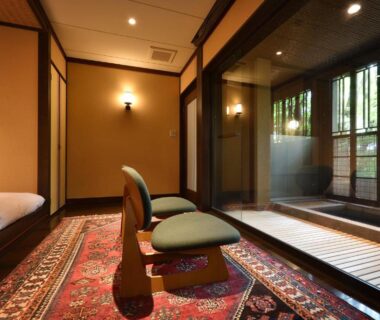 Japanese style room with low seating, futon bedding and glass wall overlooking a wooden bath