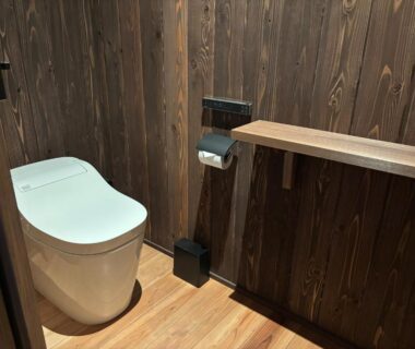 Modern toilet with wooden floor, shelf and paper holder in ryokan restroom, Kansai