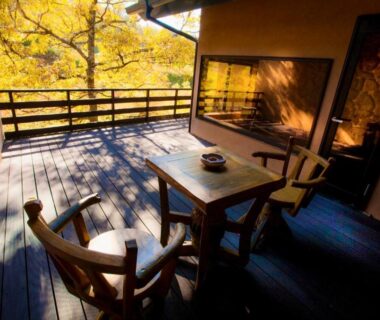 Sunlit wooden veranda with table and chairs overlooking autumn foliage at Sato no Yu Waraku in Kumamoto, Kyushu