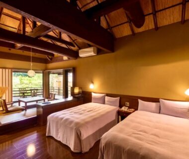 Ryokan room with twin beds, tatami seating area, shoji screens and wooden beams opening to garden view