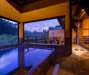 Indoor onsen bath with large windows overlooking forested hills at dusk, Sato no Yu Waraku, Kumamoto, Kyushu