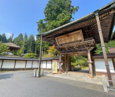 Carved wooden entrance gate of Kongo Sanmaiin with white walls and tall evergreen trees, Wakayama Kansai
