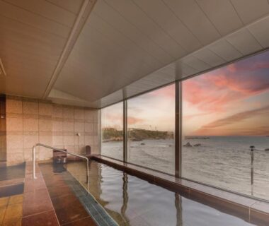 Indoor bath with floor-to-ceiling windows overlooking the sea at sunset