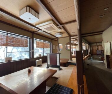 Dining area with tatami flooring, low wooden tables, zabuton cushions and bamboo blinds at Zenigame in Ishikawa