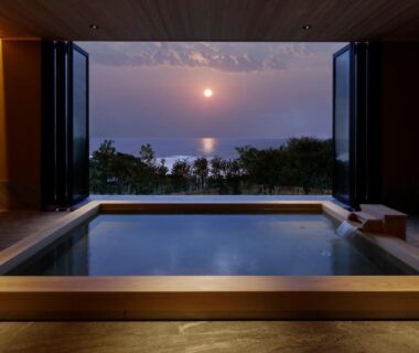 Wooden indoor onsen bath opening to sea sunset through wide sliding doors