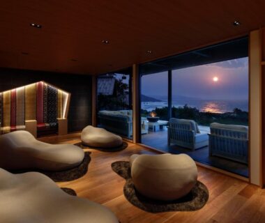 Interior lounge with organic stone-shaped seating, wooden floor and floor-to-ceiling windows overlooking coastal sunset at Sumihei Taiza Onsen Kyoto