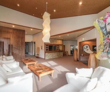 Spacious lounge with white sofas, wooden tables, pendant light and vibrant wall art at Abekura Onsen, Kanagawa