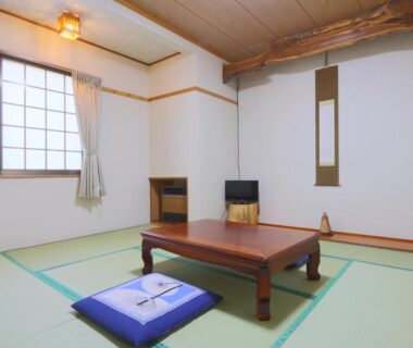 Tatami room with low table, zabuton cushion, shoji window, and small television at Suzumenoyado Yagura in Nagano