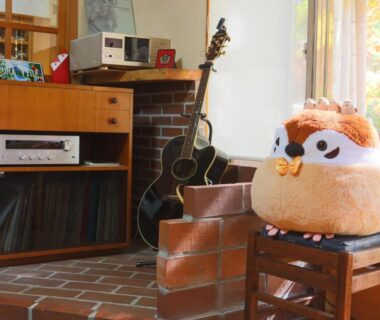 Plush owl cushion on chair beside guitar and record player near sunlit brick hearth in ryokan lounge, Nagano