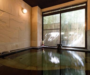 Stone-walled indoor bath with bamboo garden view at Miyabitake ryokan in Kanagawa, Japan