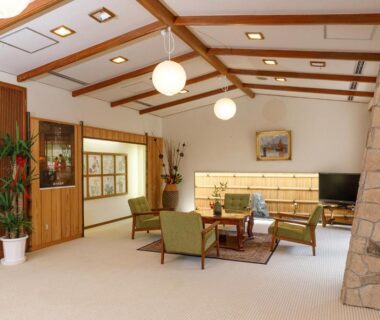 Spacious lounge with wooden beams, green sofas and stone pillar at 雅竹Miyabitake Kanagawa