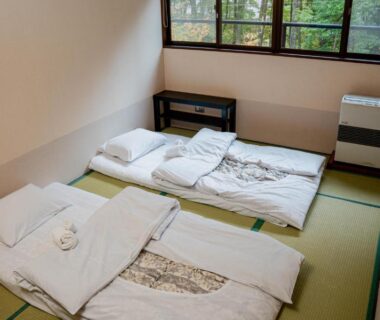 Two futons on tatami mats beside a large window with simple wooden shelving in a Nagano ryokan room