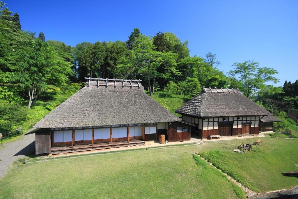 Thatched roof ryokan Kaze no Sawa Miyagi Tōhoku Two thatched roof buildings with wooden facades and grassy courtyard under clear blue sky in Miyagi, Tōhoku