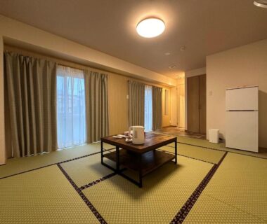 Spacious tatami room with low table, curtains, electric kettle and refrigerator at Hôtel Ekihon in Niigata