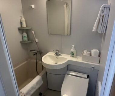 Compact unit bathroom with toilet, sink, mirror, short bathtub and wall-mounted shower, toiletries and towel rack