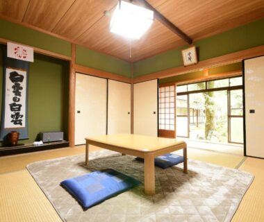 Traditional tatami room with low wooden table, zabuton cushions, shoji screens and sliding doors to a small garden