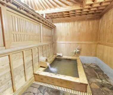 Indoor wooden bathing tub in a traditional ryokan with stone floor and wooden panel walls