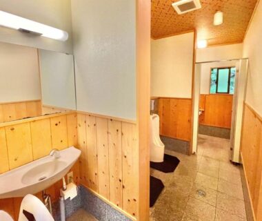 Shared washroom corridor with wooden wainscoting, sink, mirror and window-lit tiled floor