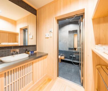 Washroom with sink, mirror, wooden paneling and doorway leading to tiled bath at Ekoin Koyasan, Wakayama