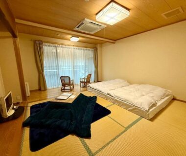 Tatami room with futon bedding, low table and two chairs by window at Kinasa no Yu, Nagano