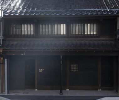 Two-story traditional wooden ryokan facade with tiled roof and lattice windows on a quiet street in Ishikawa
